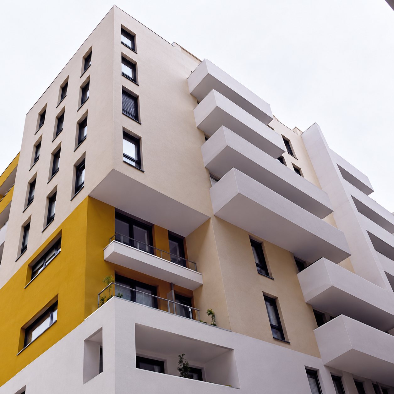 Façade d'un immeuble d'habitation contemporain blanc et jaune, avec de grands balcons en saillie, vue en contre-plongée sous un ciel clair.