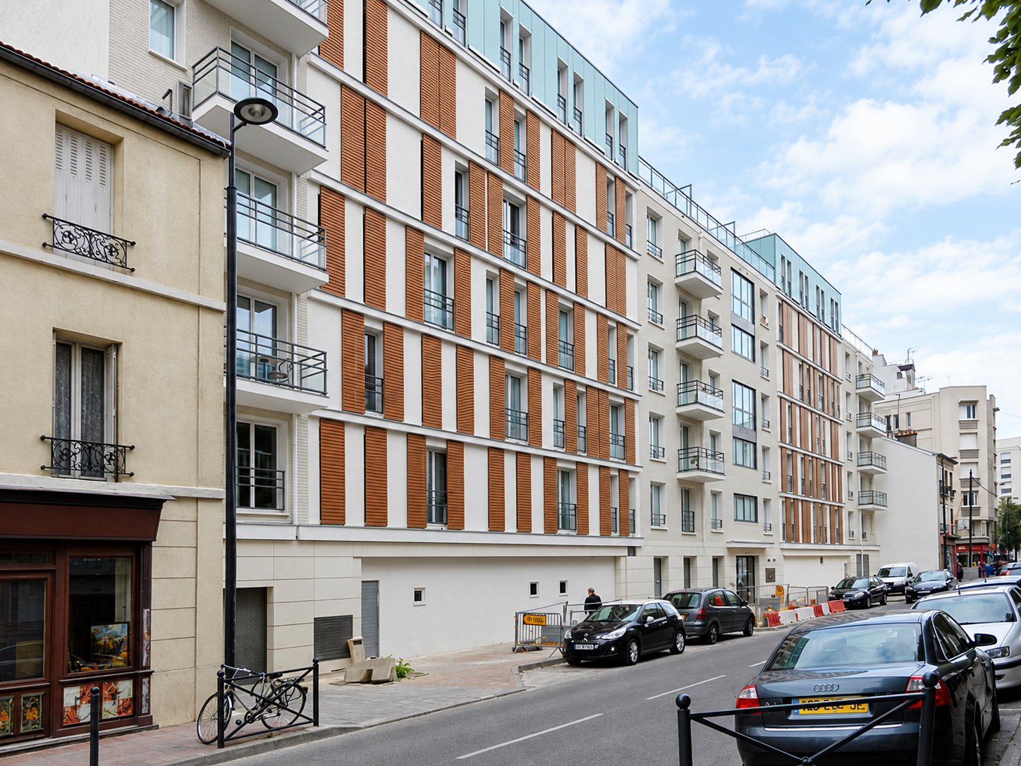 Immeuble à façade claire et bandes de briques orangées au coin d'une rue parisienne.