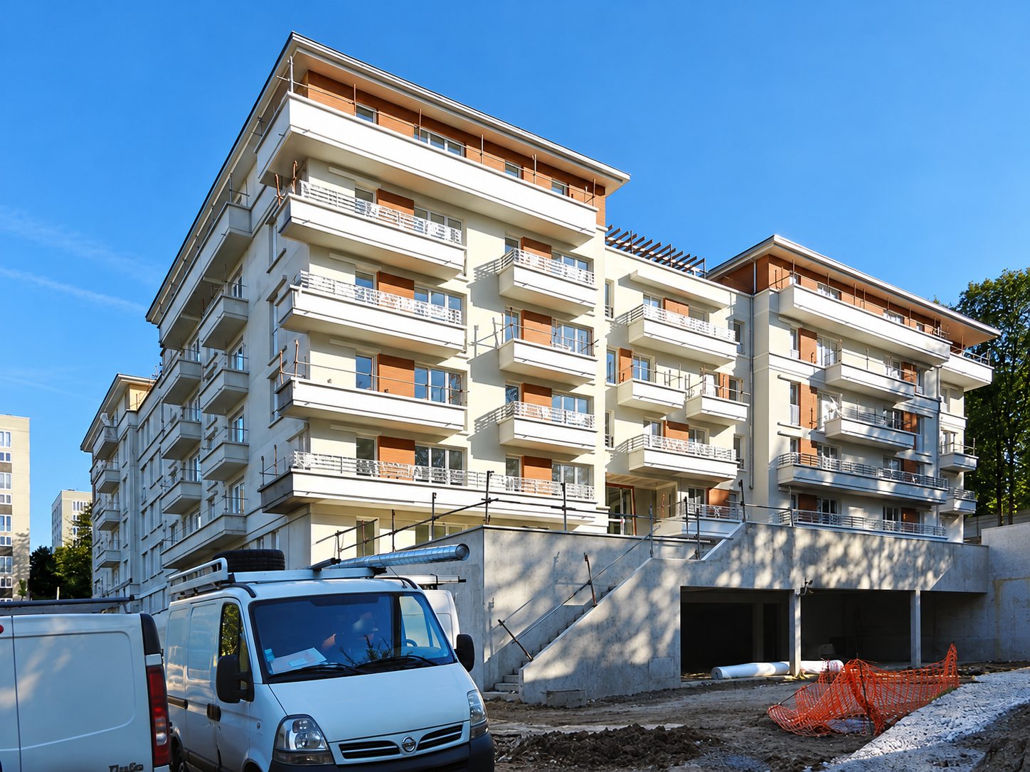 Résidence blanche à balcons et loggias sur un sous-sol de garage, avec une camionnette blanche devant.