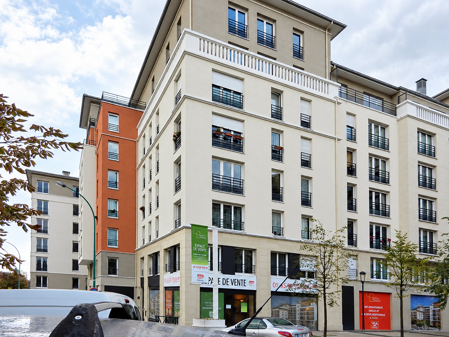 Immeubles de couleur crème à balcons et commerces en rez-de-chaussée, au bord d'une rue.